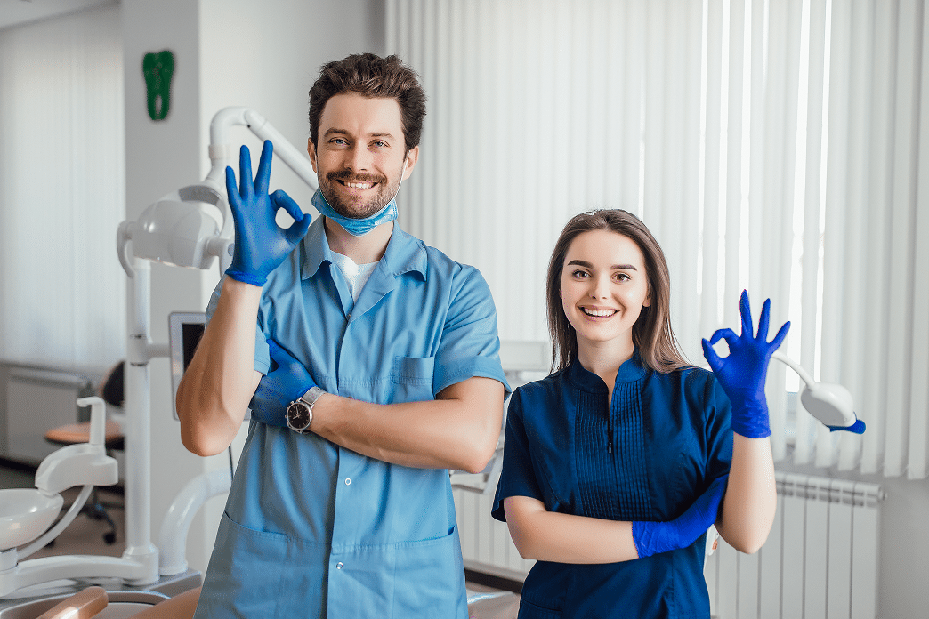 photo-smiling-dentist-standing-with-arms-crossed-with-her-colleague-showing-okay-sign